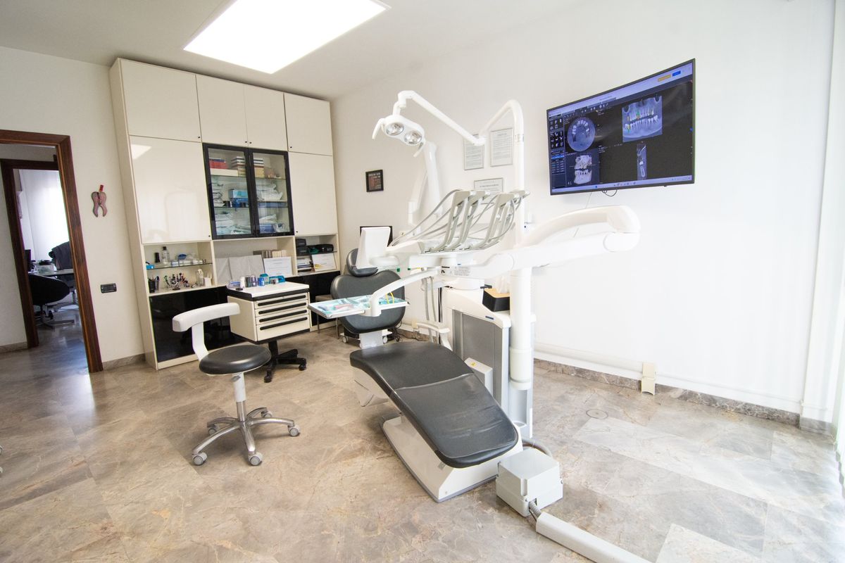 Sala cure con riunito, carrello degli strumenti e monitor a parete con immagini radiografiche